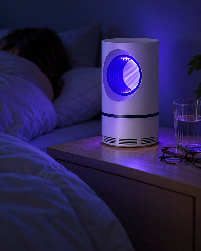 La lámpara prendida con su luz violeta en un velador, junto a una cama donde alguien duerme