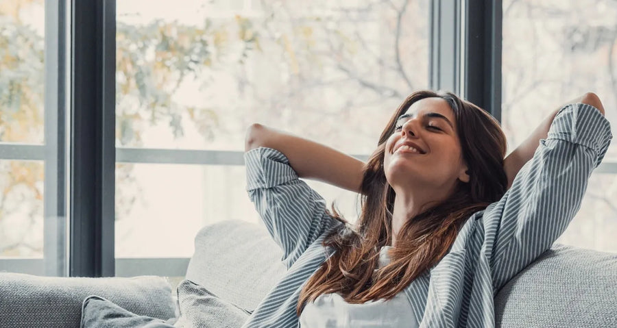 Una mujer estirándose relajada en el sofá, junto a una ventana